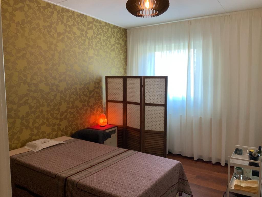 Behandelkamer met massagebed, kamerscherm en zoutlamp tegen het gouden ginkgo-behang.