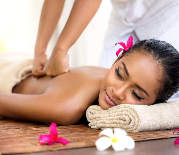 Rugmassage met olie, met een opgerolde handdoek en bloemen ernaast.