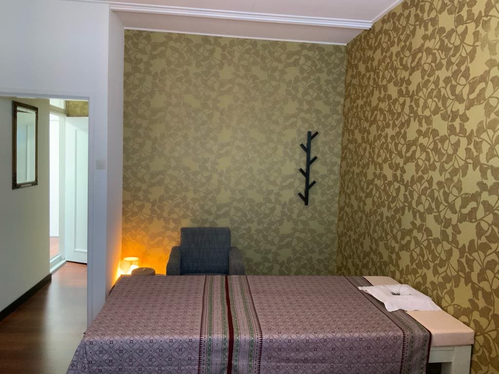 Het massagebed met een fauteuil ernaast en warm licht tegen het ginkgo-behang.