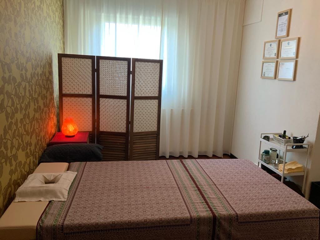De behandelkamer met opgemaakt bed, kamerscherm en de diploma's aan de wand.